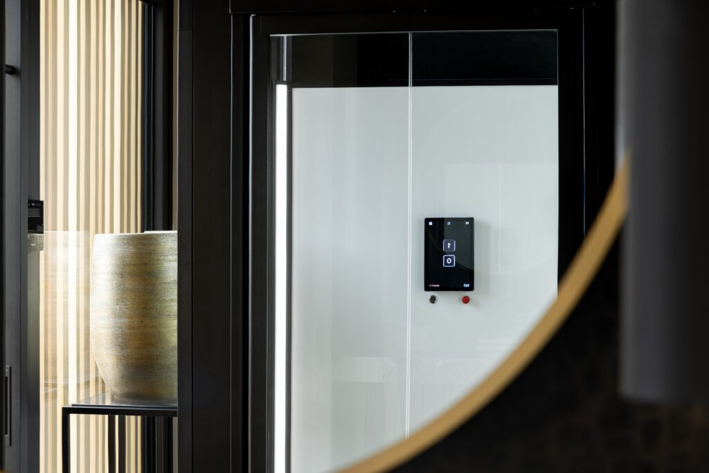Voorzijde van een luxe glazen lift met wit achterpaneel en digitaal bedieningsscherm.