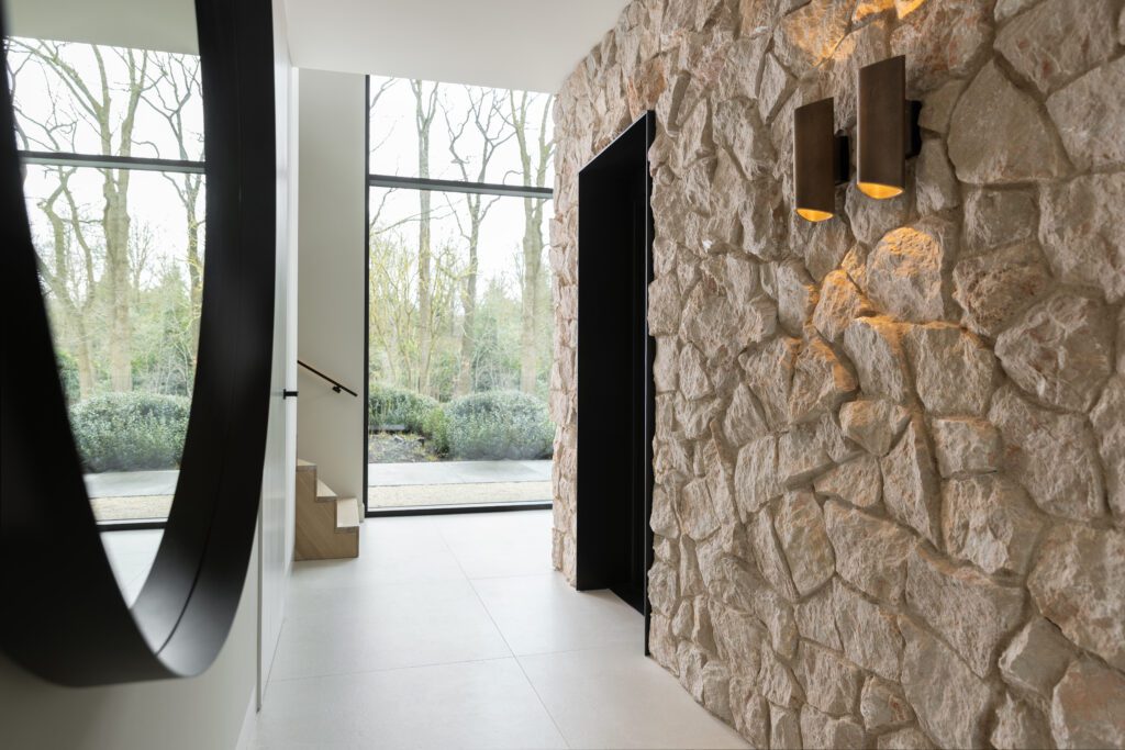 Moderne hal met natuurstenen wand, zwarte lift en warm wandlicht.