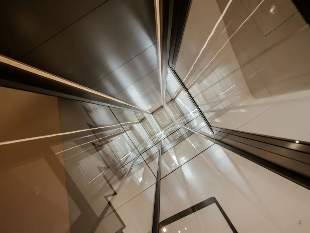 Binnenzijde van een moderne glazen lift met stalen frame en spiegelende wanden in een luxe woning.